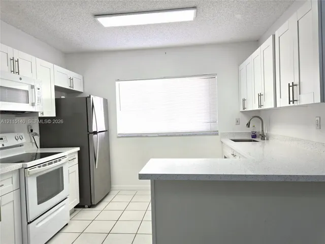 Kitchen featuring white shaker-style cabinetry, solid-surface countertops, tile flooring, stainless steel appliances, and a gooseneck faucet