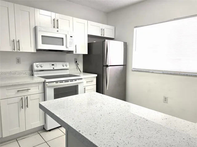 Kitchen featuring white shaker-style cabinetry, solid-surface countertops, a breakfast bar, and stainless steel appliances