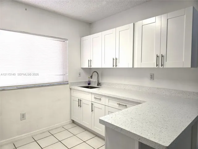 White Shaker-style cabinetry with satin nickel hardware, speckled quartz countertops, under-mount stainless steel sink, gooseneck faucet, and ceramic tile flooring
