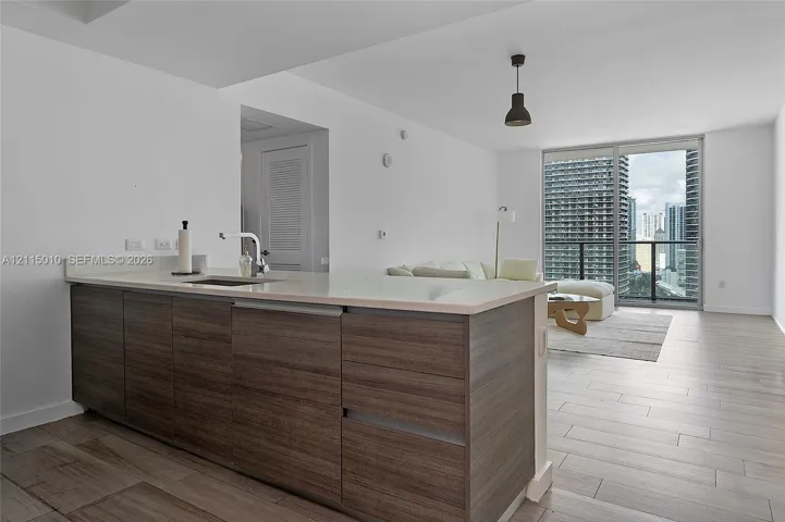 Kitchen island featuring wood-finish cabinetry, solid-surface countertop, and an undermount sink, complemented by light-toned tile flooring and expansive sliding glass doors