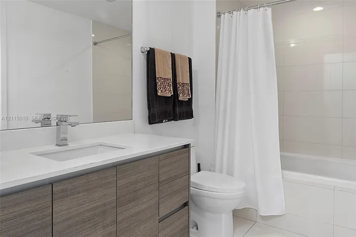 Bathroom featuring a flat-panel wood-finish vanity, rectangular undermount sink, stone-surface countertop, chrome single-handle faucet, and full-height tiled shower surround