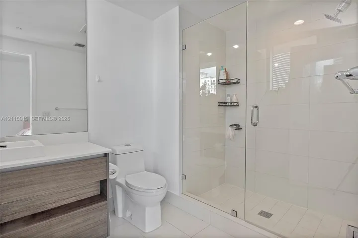 Bathroom featuring a wood-finish vanity with an integrated basin, large-format tile flooring, a glass-enclosed walk-in shower with light-toned tile surround, and recessed lighting