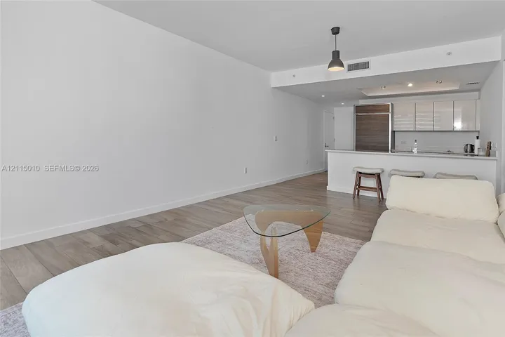 Open-concept living space featuring wood-finish flooring, kitchen with high-gloss cabinetry, integrated refrigerator, and a breakfast bar