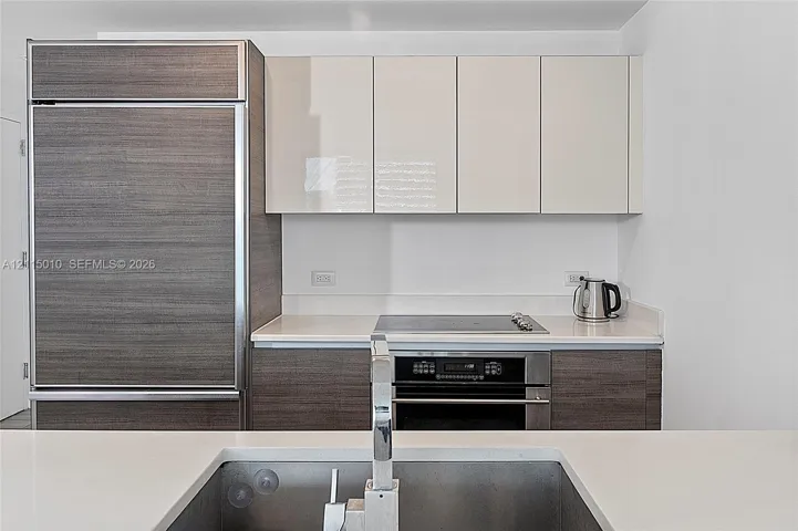 Kitchen featuring high-gloss cabinetry, wood-finish paneling, an integrated refrigerator, a built-in oven with a cooktop, and an undermount sink with a chrome faucet