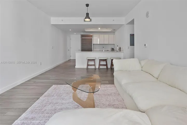 Open-concept interior featuring wood-finish flooring, a kitchen island with stone countertops, modern flat-panel cabinetry, and a minimalist pendant light fixture