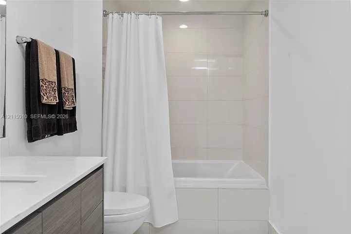 Bathroom featuring a floating vanity with stone countertop, recessed lighting, and a tub with large-format wall tile surround