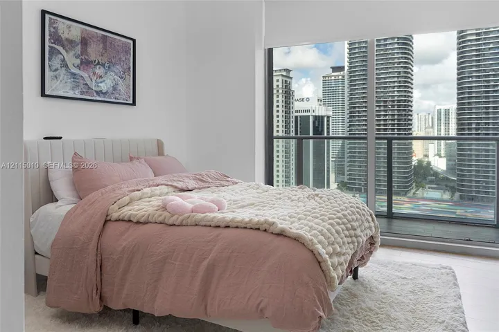 Floor-to-ceiling windows featuring urban skyline exposure, integrated balcony access with dark-framed railing, and light-toned hard-surface flooring