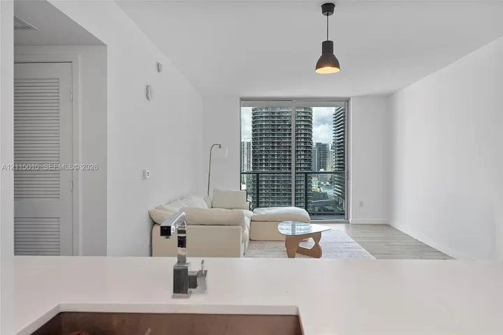 Solid surface countertop with a single-handle chrome faucet, floor-to-ceiling glass sliding doors, wood-finish flooring, and a single black industrial-style pendant light