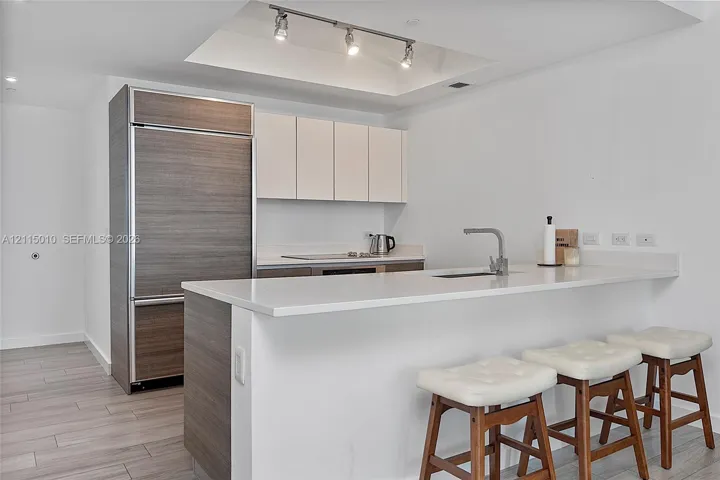 Kitchen featuring a stone-surface island with an integrated sink, custom cabinetry with wood-finish paneling, a paneled refrigerator, recessed ceiling lighting, and wood-finish flooring