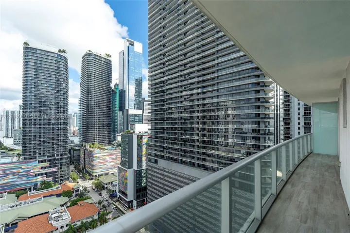 Covered balcony featuring wood-finish flooring, glass panel railing, and high-rise urban surroundings