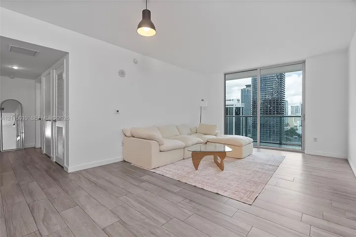 Wood-finish flooring, floor-to-ceiling glass sliding doors, private balcony with metal railing, and pendant lighting