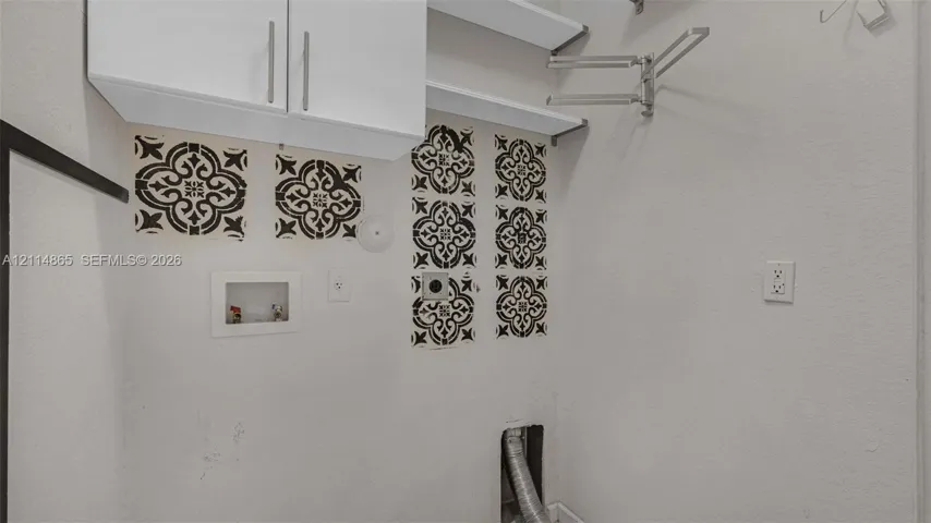 Utility area featuring white overhead cabinetry, open shelving, decorative tile accents, and a retractable wall-mounted garment rack