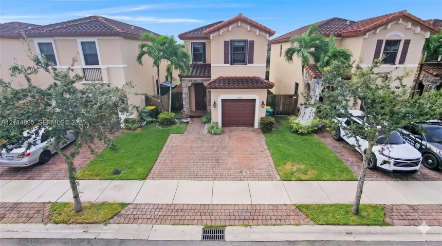 Stucco exterior featuring a tiled roof, stone veneer accents, integrated garage, and paved driveway