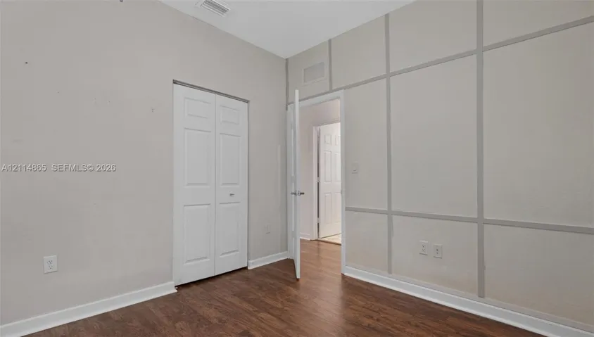 Room featuring wood-finish flooring, decorative wall molding, and a bi-fold closet door