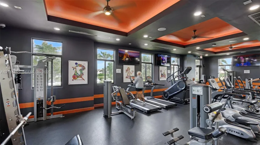 Fitness center featuring recessed tray ceilings with accent lighting, multiple ceiling fans, recessed lighting, and large windows