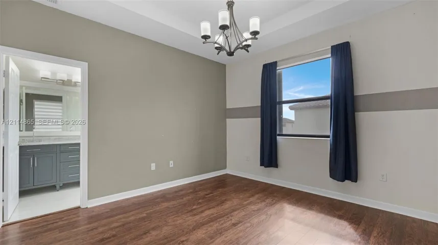 Room featuring wood-finish flooring, a tray ceiling, and a multi-arm chandelier