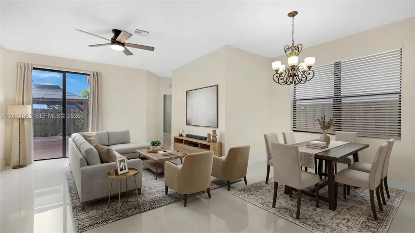 Virtually staged. Open-concept floor plan featuring light-toned flooring, an ornate multi-arm chandelier, a ceiling fan with integrated lighting, and glass sliding doors