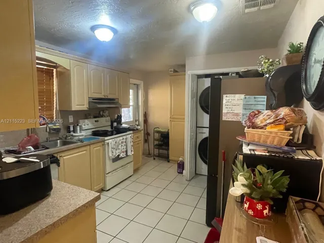 Kitchen featuring light-toned cabinetry, solid-surface countertops, tile flooring, and a dedicated laundry area with stacked washer and dryer