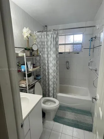 Bathroom featuring white tile wall cladding with decorative black inlay, a white vanity with an integrated basin, a standard soaking tub, and a window with textured privacy glass