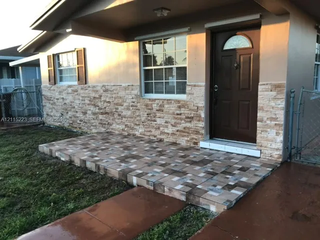 Exterior entry featuring a textured stone veneer facade, a tiled porch, and an arched-glass entry door with a brass-finish door knocker