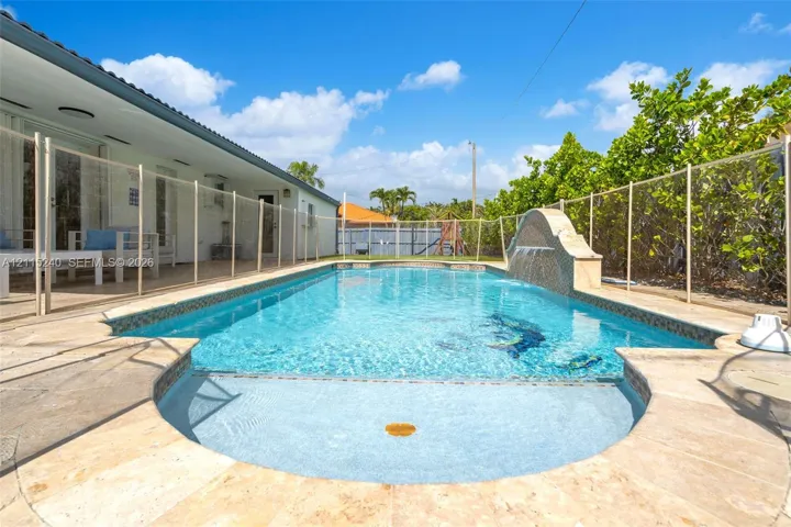 In-ground swimming pool with stone-tiled decking, integrated water feature, and a shallow sun shelf