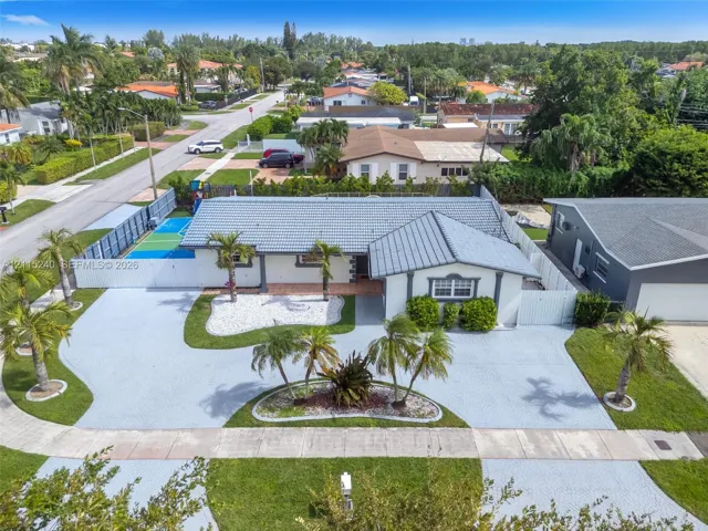 Single-story residence featuring a tile roof, an expansive paved driveway, a gated sports court, and manicured landscaping with mature palm​​‌​​​​‌​​‌‌​‌‌​​​‌‌​‌​‌​‌​​​‌​​ trees