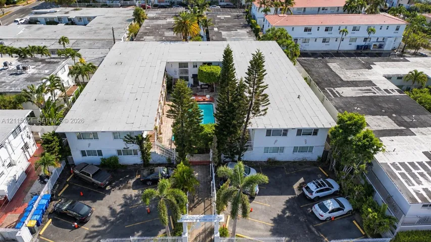 U-shaped multi-unit building featuring a central courtyard with an in-ground swimming pool, mature perimeter landscaping, and dedicated surface parking