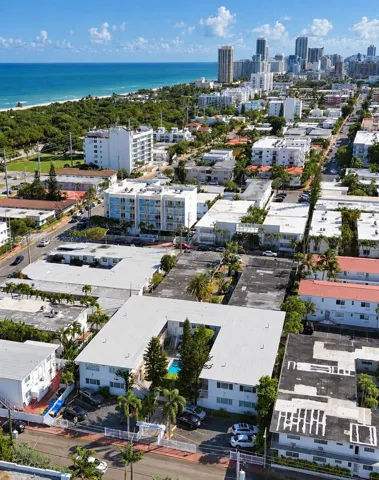 Aerial perspective featuring a multi-unit residential structure with an internal courtyard swimming pool, palm landscaping, and dedicated surface parking