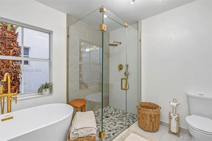 Freestanding soaking tub with a brass-finish floor-mounted faucet, frameless glass-enclosed shower with a pebble stone floor, and brass-finish shower fixtures