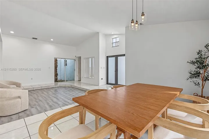 Vaulted ceilings with recessed lighting, wood-finish flooring, large-format tile flooring, multi-pane glass entry doors, and triple-pendant glass lighting fixtures
