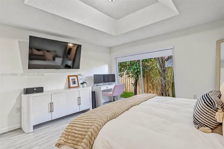 Tray ceiling, light-toned wood-finish flooring, white built-in cabinetry with metal pulls, and sliding glass doors
