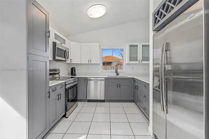 Kitchen featuring two-tone shaker cabinetry, solid-surface countertops, stainless steel appliances, ceramic tile flooring, and integrated wine storage