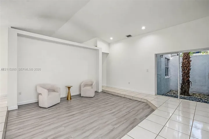 Interior featuring vaulted ceilings, wood-finish flooring, recessed lighting, and a sliding glass door providing external access to a walled courtyard