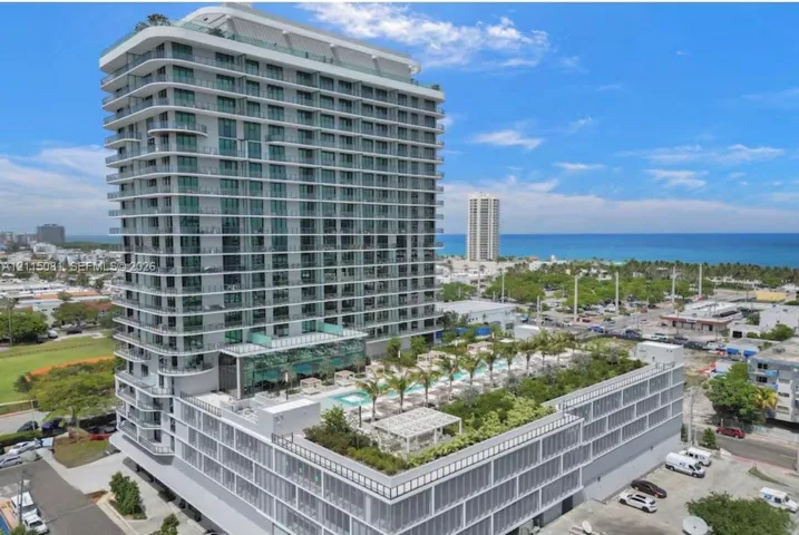 High-rise residential tower featuring a glass-facade exterior, wrap-around balconies, and an elevated terrace level with an outdoor pool, manicured landscaping, and pergolas