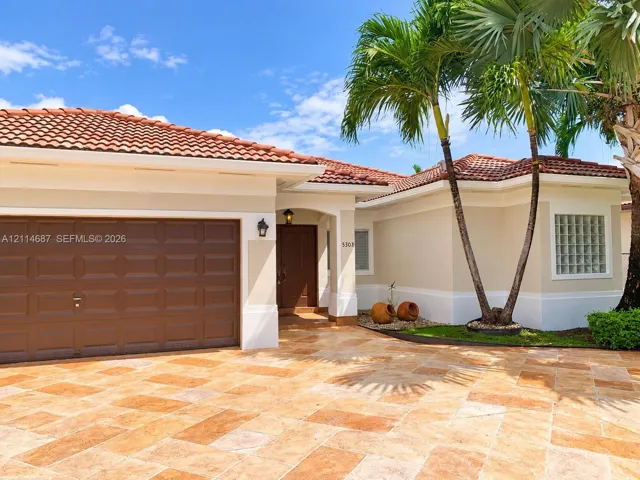 Exterior facade featuring a terracotta-tiled roof, stone-paver driveway, single-panel garage door, and glass block window accents