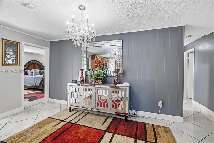 Interior space featuring vertical paneled accent wall, neutral tile flooring in a diamond pattern, and a tiered crystal chandelier