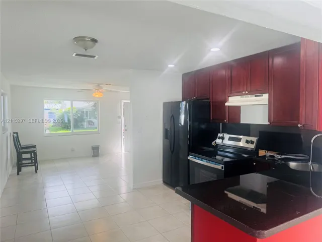 Kitchen featuring dark-toned cabinetry, solid surface countertops, a black finish range, a matching black refrigerator, and tile flooring