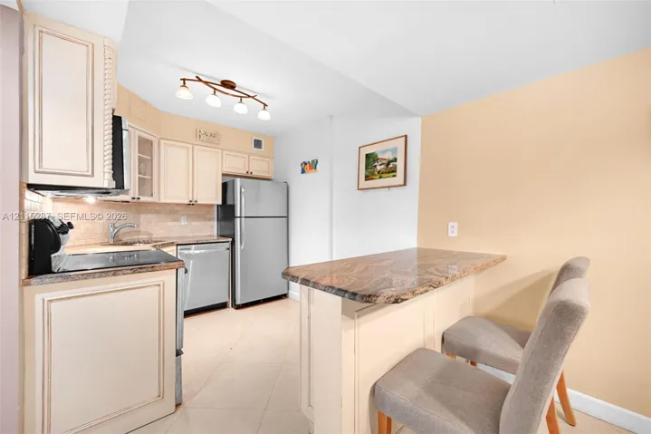 Kitchen featuring custom cabinetry, stone-surfaced countertops, a stone-tiled backsplash, stainless steel appliances, and a breakfast bar