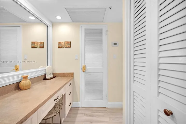 Built-in vanity featuring a solid-surface countertop, full-width wall mirror, wood-finish flooring, and white louvered closet doors