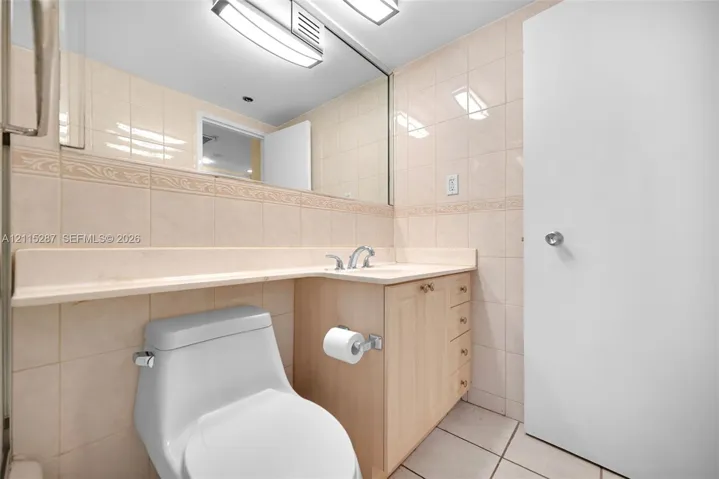 Bathroom featuring a wood-finish vanity with an integrated countertop and sink, wall-to-wall mirror, tiled walls with decorative trim, and overhead task lighting