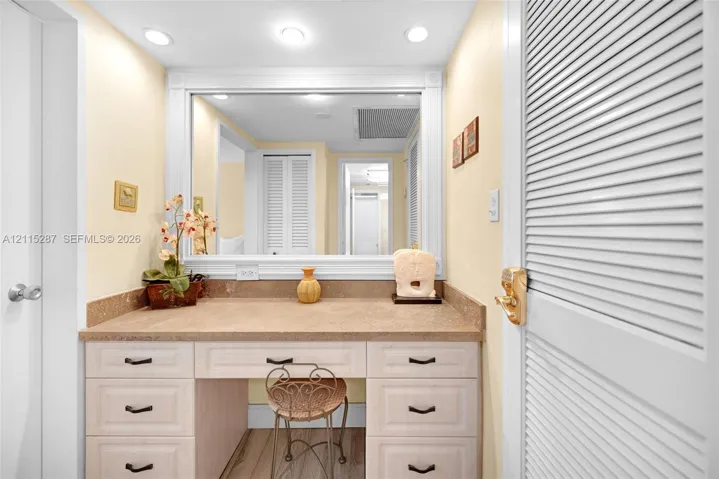 Built-in vanity featuring a stone-finish countertop, light-toned cabinetry, recessed lighting, and an expansive wall-mounted mirror with decorative trim