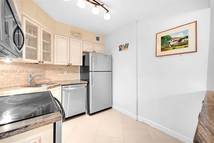 Kitchen featuring cabinetry with glass-panel upper doors, stone-finish countertops, stainless steel appliances, tiled backsplash, and light-toned tile flooring