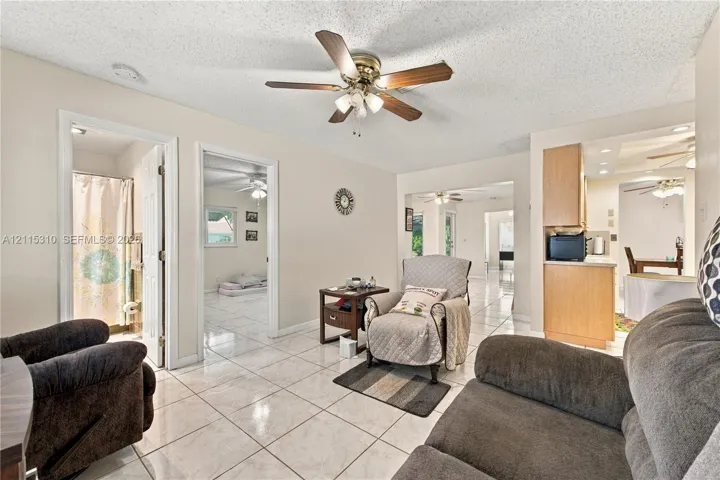 Open-concept interior featuring light-colored ceramic tile flooring, a ceiling fan with integrated lighting, and natural wood cabinetry