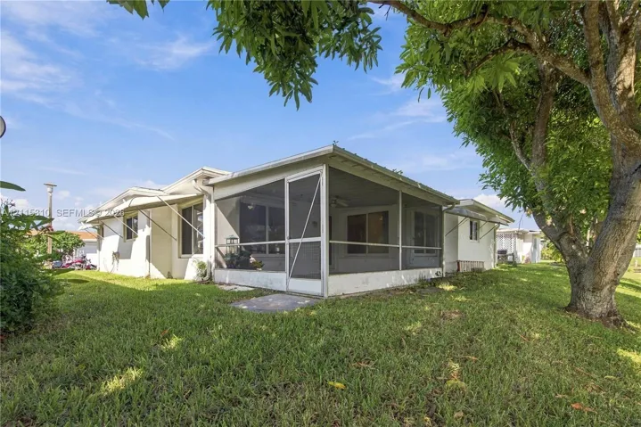 Exterior featuring white siding, a screened-in lanai, metal awnings, and mature landscaping