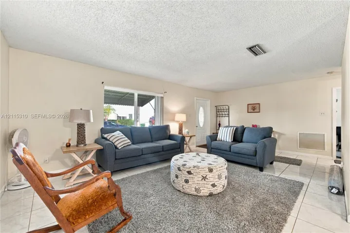 Living area featuring large format tile flooring, neutral wall paint, and a front entry door with an oval glass insert