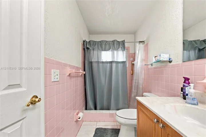 Bathroom featuring pink ceramic wall tiling, wood-finish cabinetry, a white countertop with an integrated sink, and a porcelain tub with a tiled surround