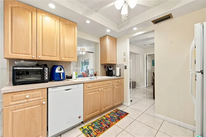 Kitchen featuring wood cabinetry, integrated white dishwasher, neutral-tone countertops, tile flooring, and recessed ceiling lighting