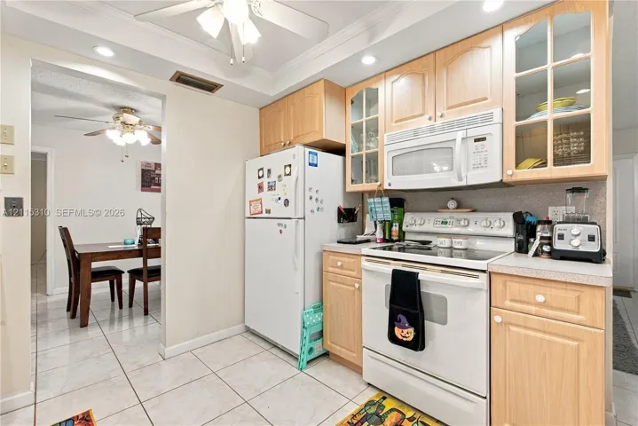 Kitchen featuring light wood-finish cabinetry, glass-front upper cabinet doors, white appliances, and tiled flooring