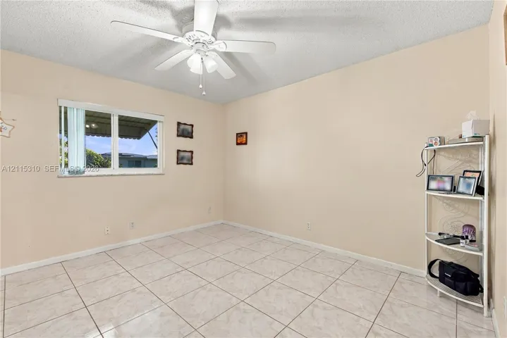 Neutral-toned room featuring ceramic tile flooring, a multi-blade ceiling fan with integrated lighting, and a single-pane sliding window with vertical blinds