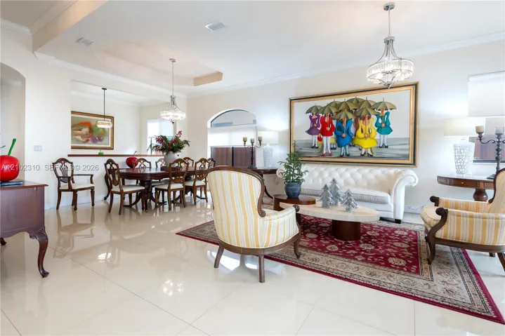 Open-concept living and dining area featuring polished tile flooring, recessed tray ceilings, and dual decorative chandeliers